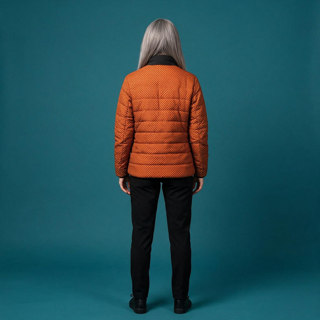 A model viewed from the back wearing a textured orange quilted puffer jacket with black trim, paired with black pants, set against a solid teal studio background.