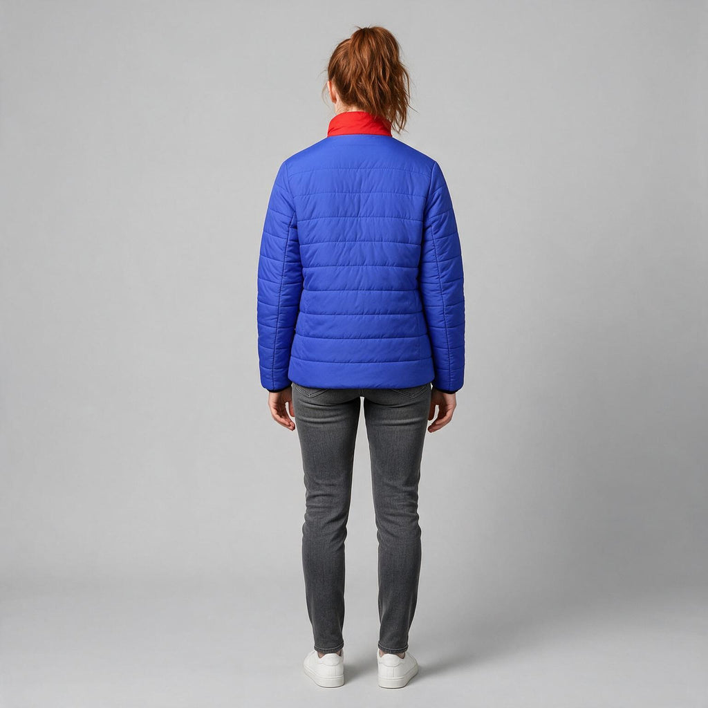 A person shown from the back wearing a bright royal blue quilted puffer jacket with a contrasting red collar, paired with dark gray jeans and white sneakers, against a light gray studio background.