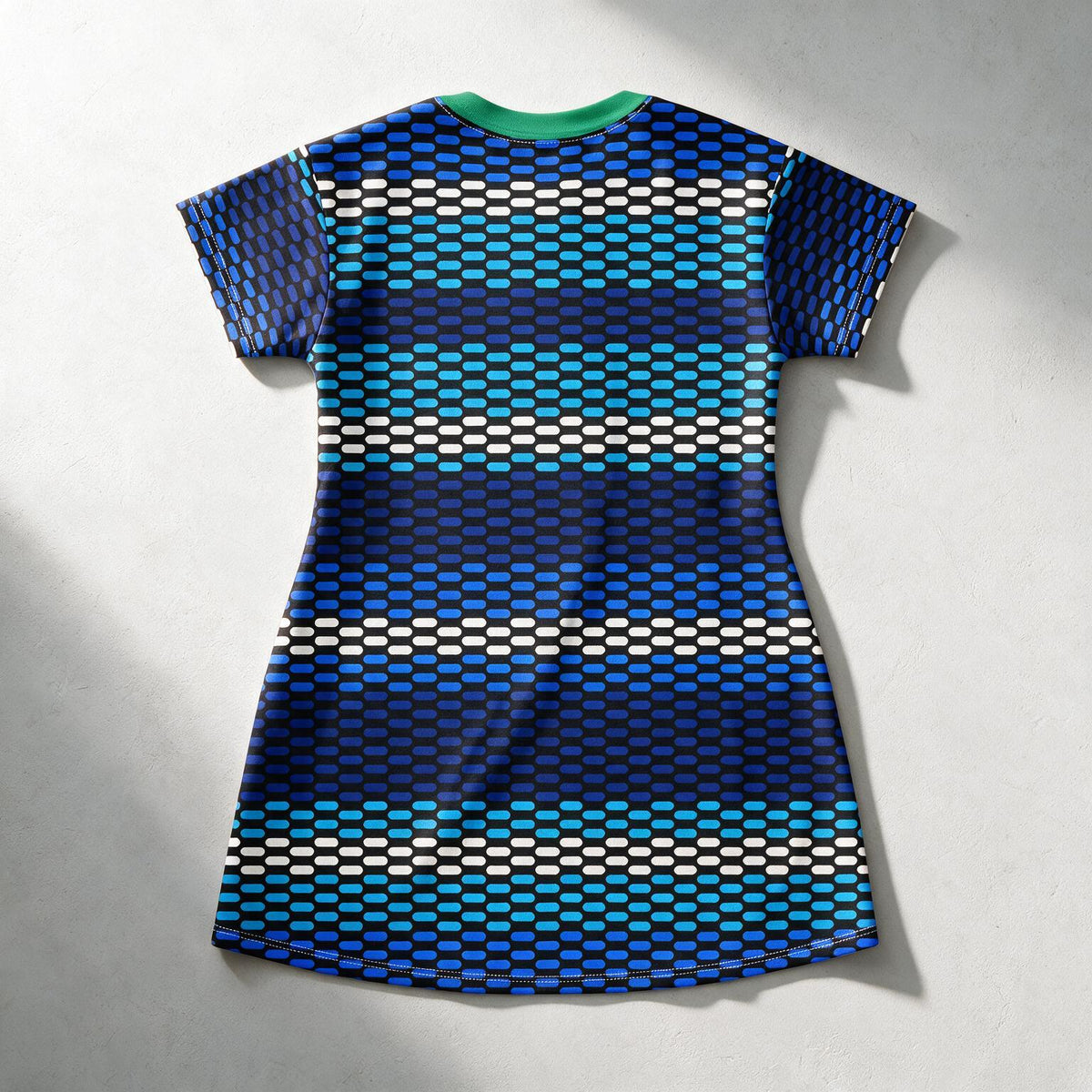 A short-sleeve t-shirt dress with a geometric pattern of horizontal stripes in shades of blue, teal, black, and white, featuring a contrasting green crew neck, shown from a top-down view on a textured gray background.
