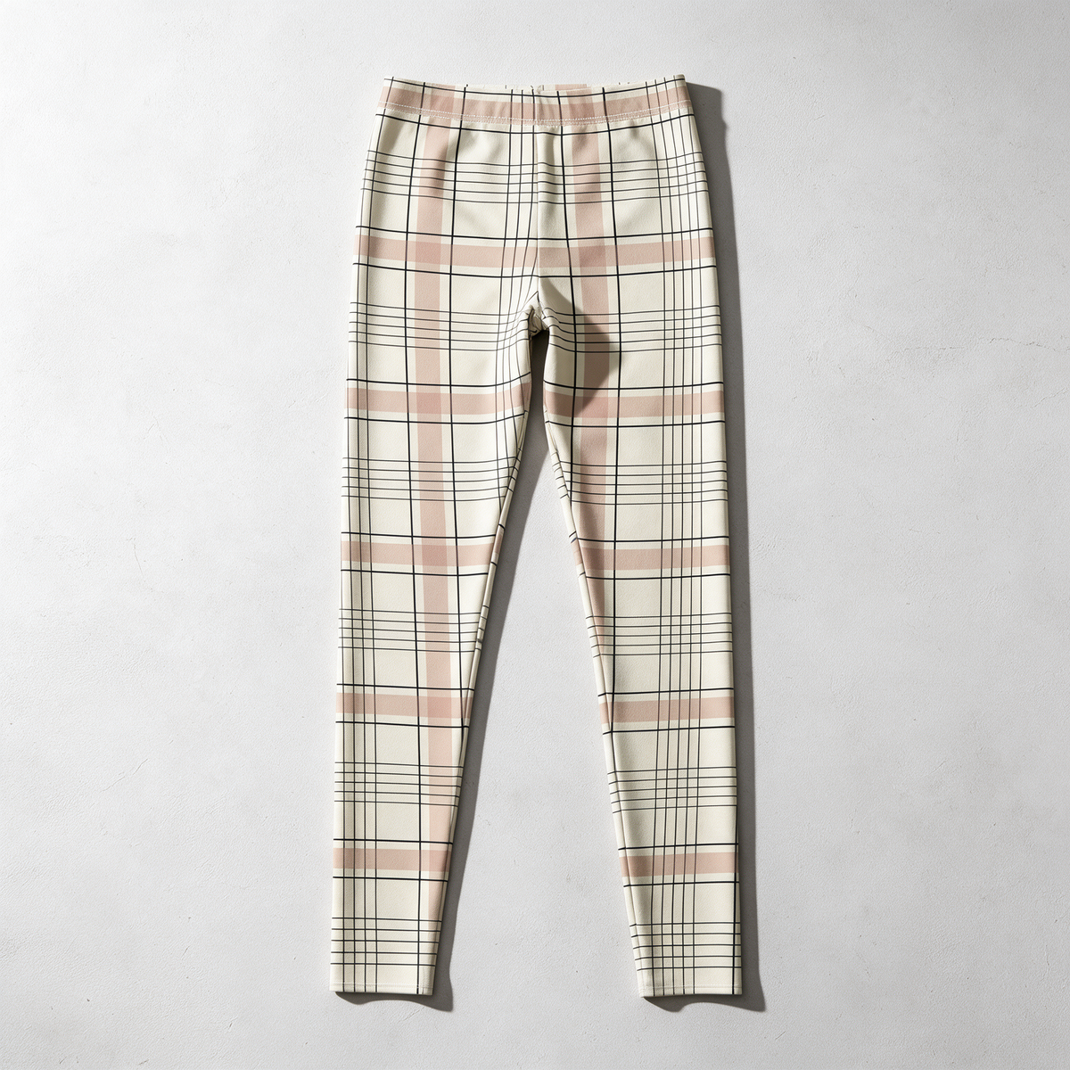 A pair of women's cropped leggings in a cream base with a pink plaid pattern and thin black grid lines, laid flat against a light gray textured background.
