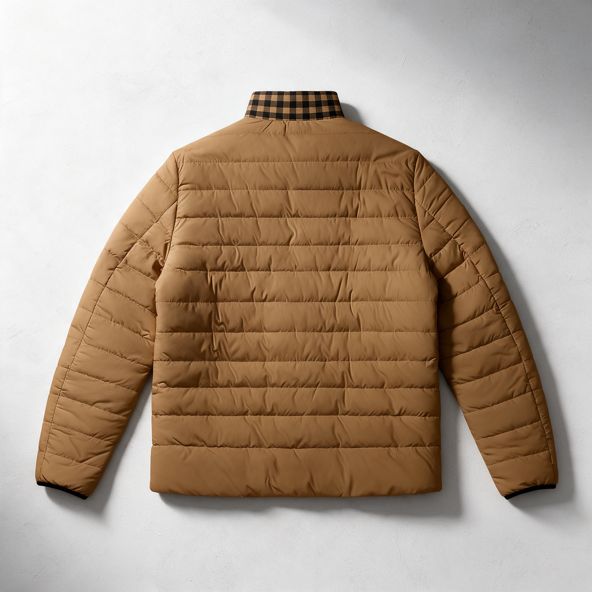 A tan quilted puffer jacket shown from the back, featuring horizontal stitching and a black and brown plaid collar, laid flat against a light gray background.