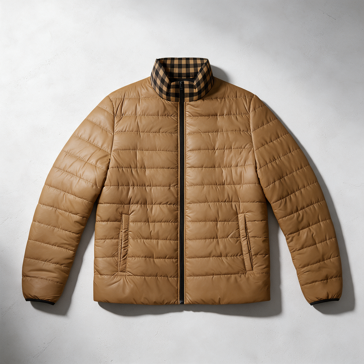 A tan quilted puffer jacket with a black and brown plaid collar, laid flat on a light gray textured background.
