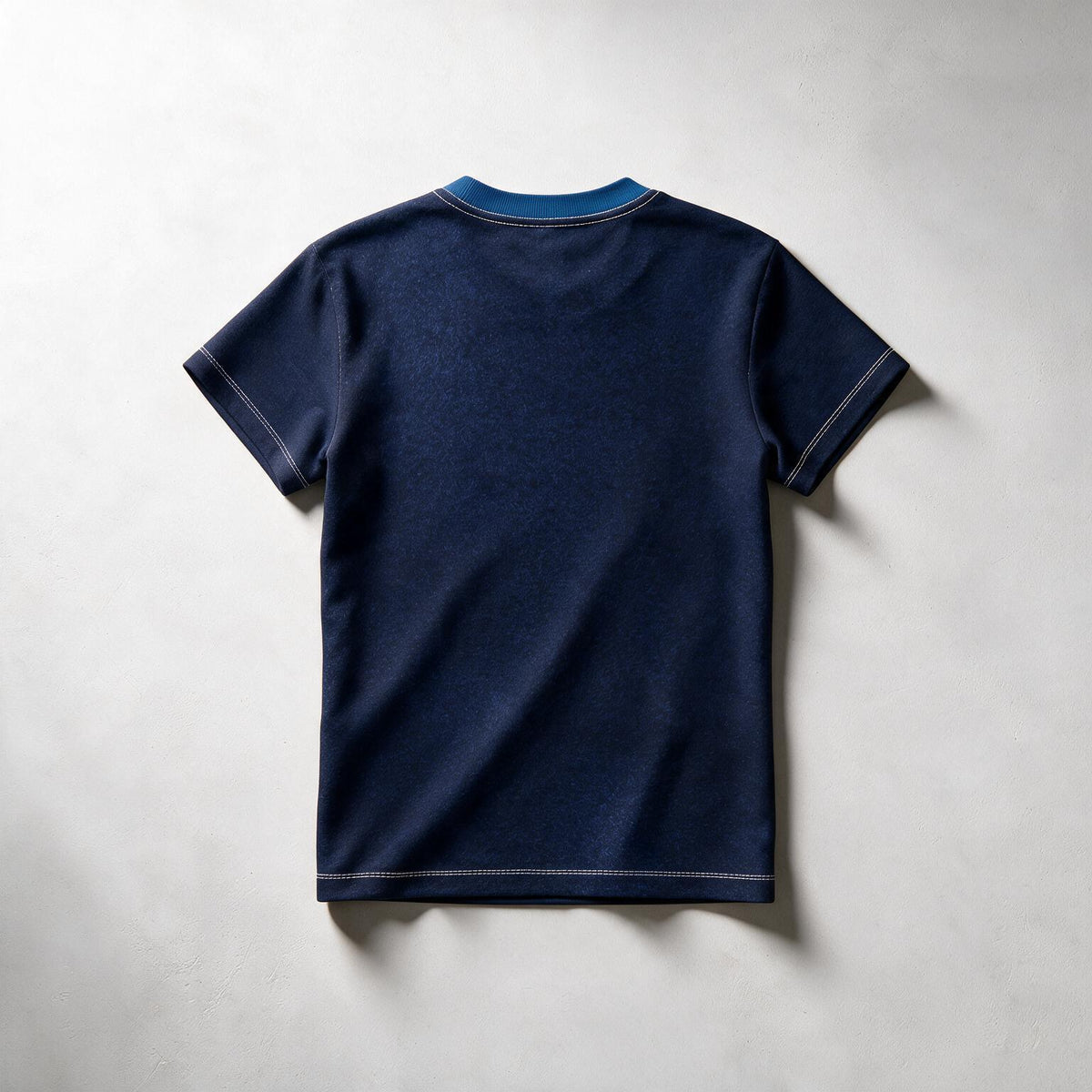 A dark navy blue short-sleeve t-shirt shown from the back, laid flat on a light gray textured background. The shirt features a contrasting light blue inner collar and subtle light gray contrast stitching.