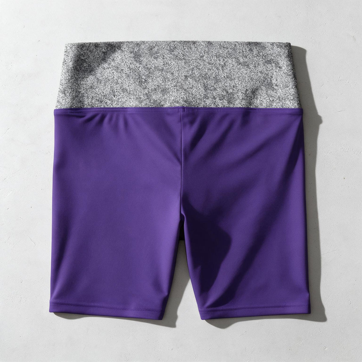 Purple and gray color-blocked athletic shorts laid flat on a light gray textured background.