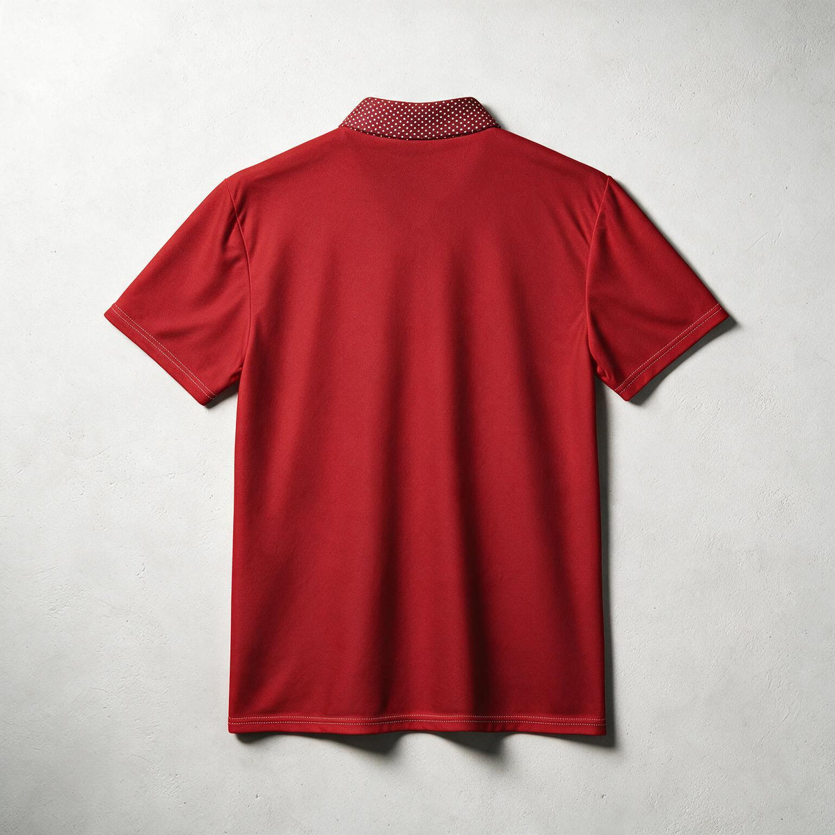 A red short-sleeve polo shirt shown from the back, laid flat against a light gray textured background. The collar features a contrasting red and white patterned lining.
