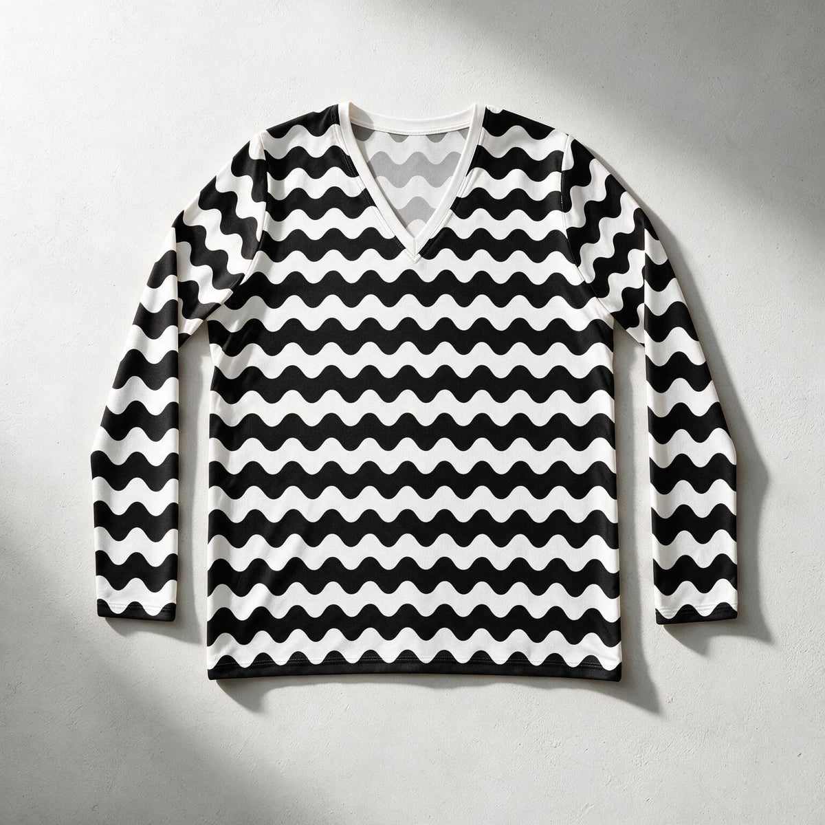 A long-sleeve V-neck sweater with a bold black and white wavy stripe pattern, laid flat against a light gray textured background.