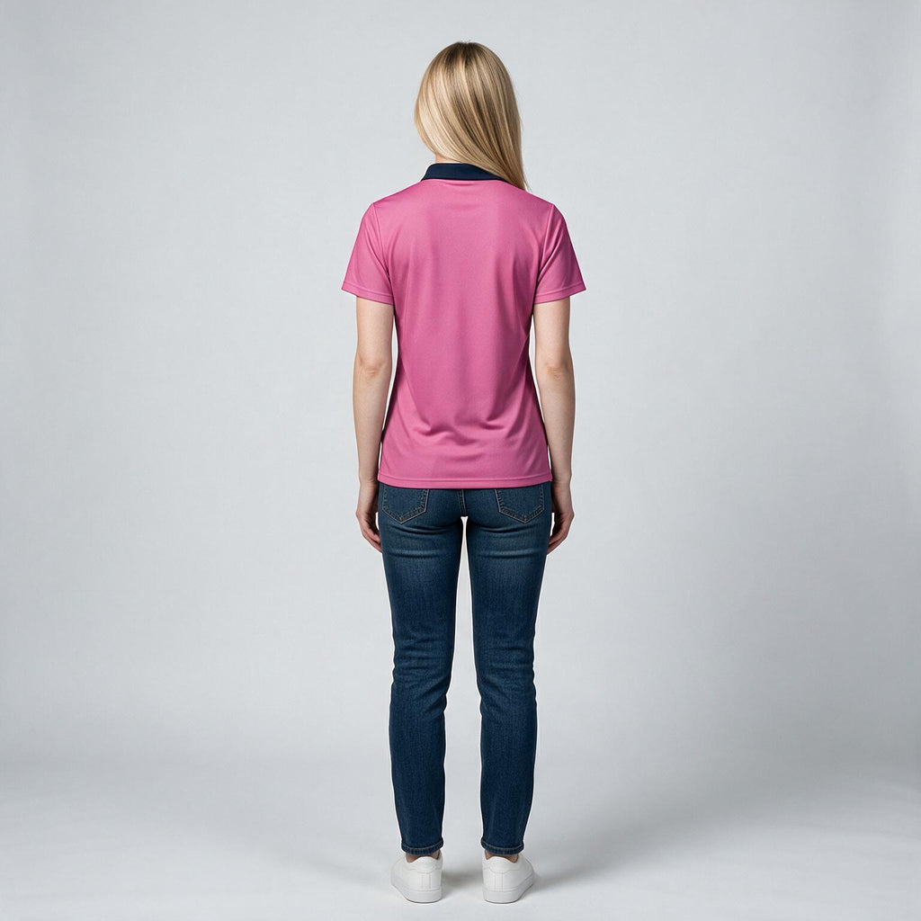A woman viewed from behind wearing a pink short-sleeve polo shirt with a dark navy collar, paired with dark blue jeans and white sneakers, against a light gray studio background.
