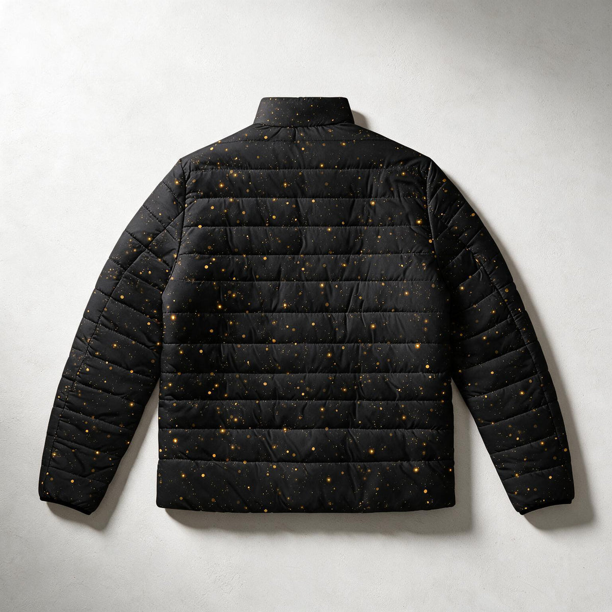 A black quilted puffer jacket with a gold speckled star pattern, shown from the back against a light gray textured background.