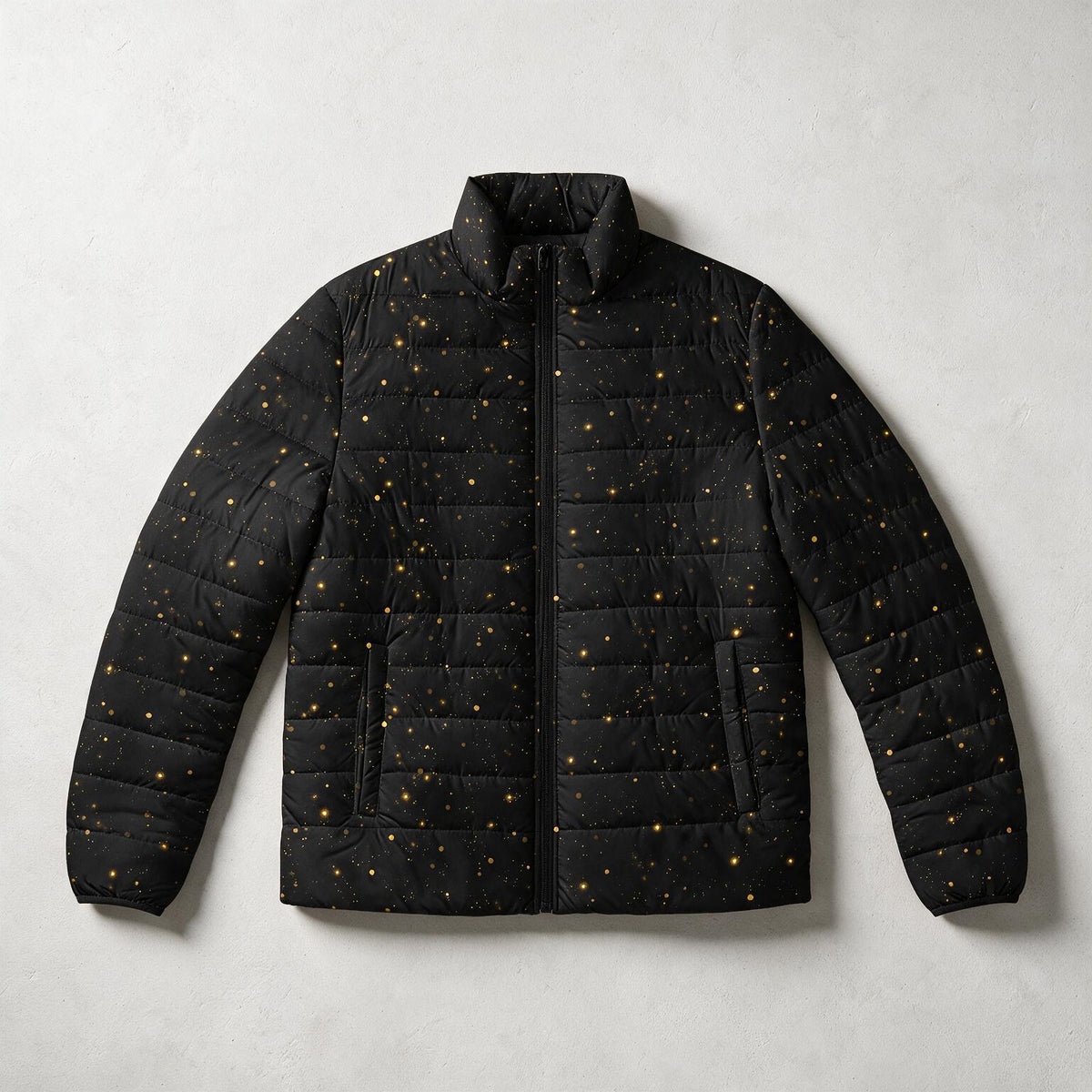 A black quilted puffer jacket with a subtle gold speckled star pattern, laid flat against a light gray textured background.