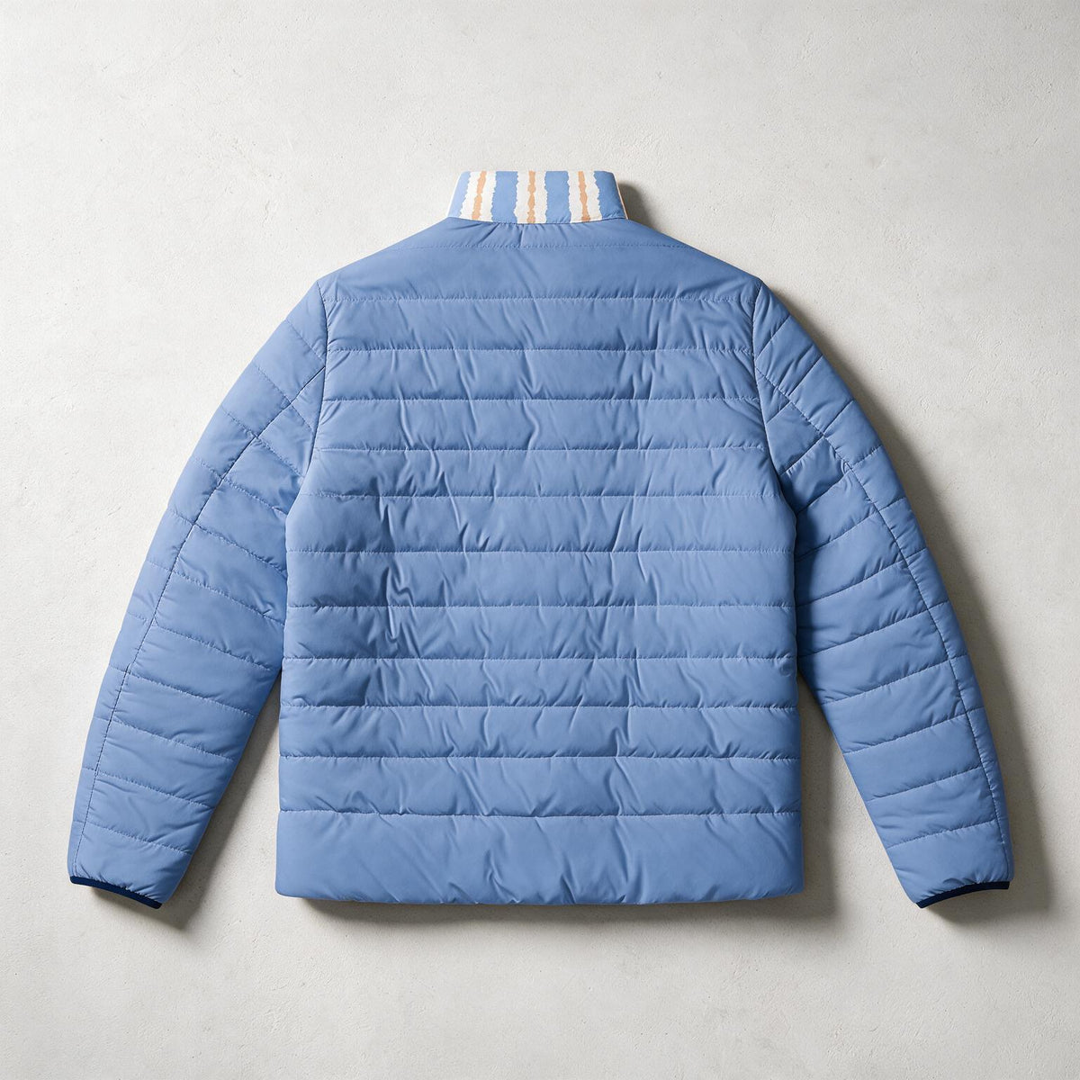 A light blue puffer jacket shown from the back, laid flat on a textured light gray background. The jacket features horizontal quilting, long sleeves, and a striped collar with white and yellow stripes.
