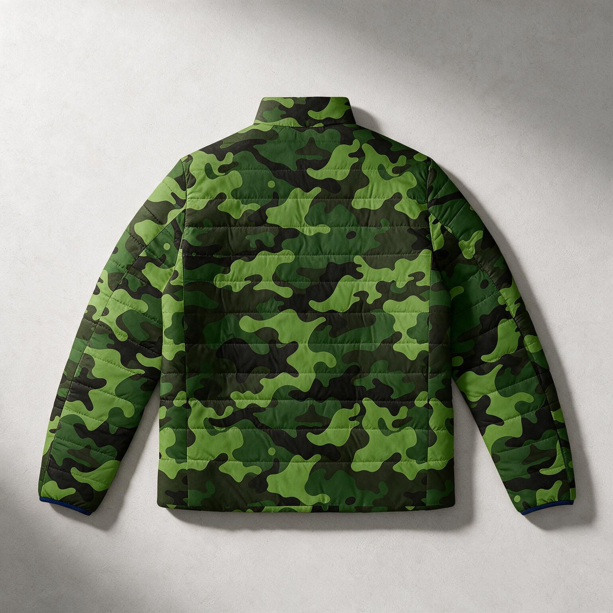 A green camouflage puffer jacket shown from the back, laid flat against a light gray textured background.