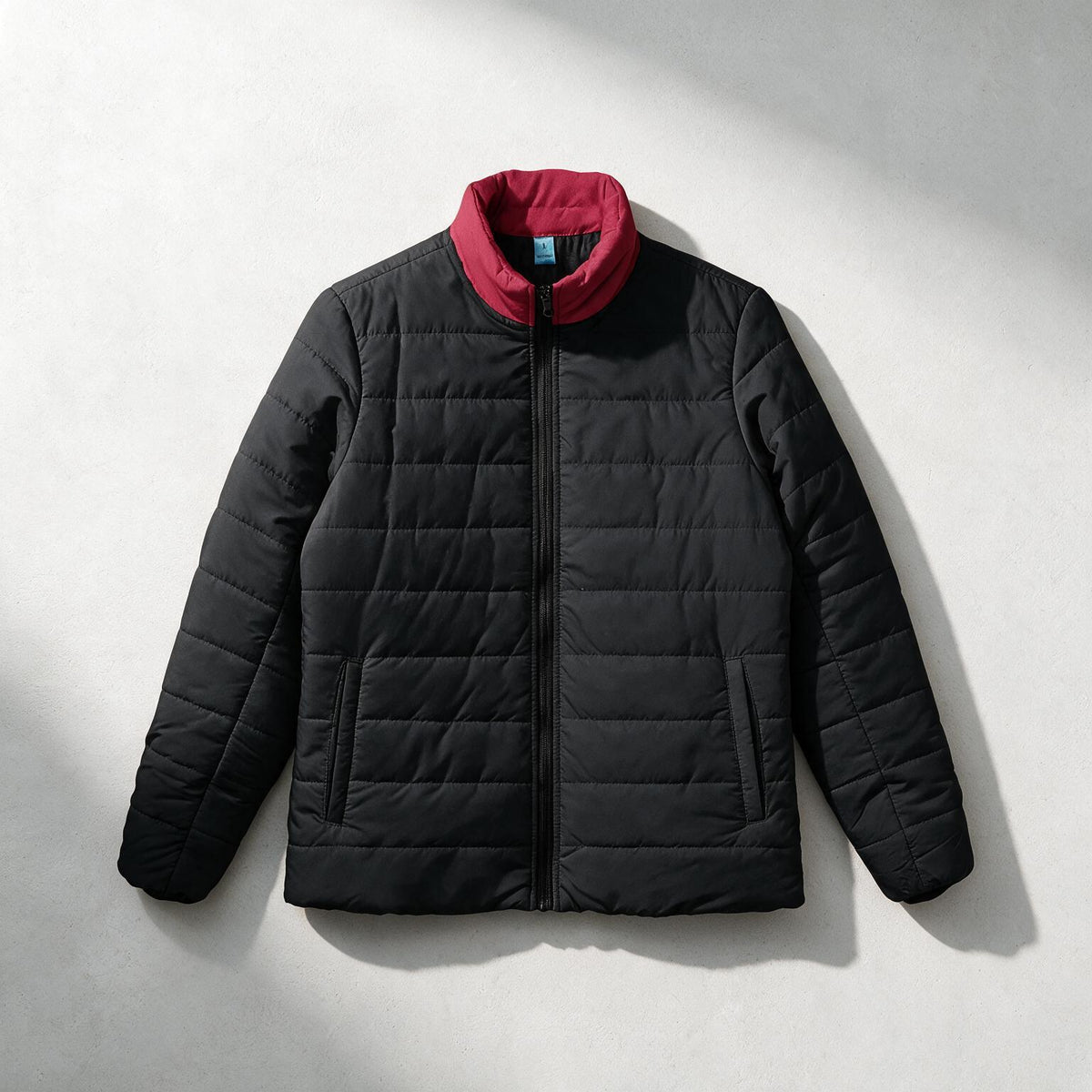 A black quilted puffer jacket with a contrasting red inner collar, displayed flat against a light gray background with soft shadows.