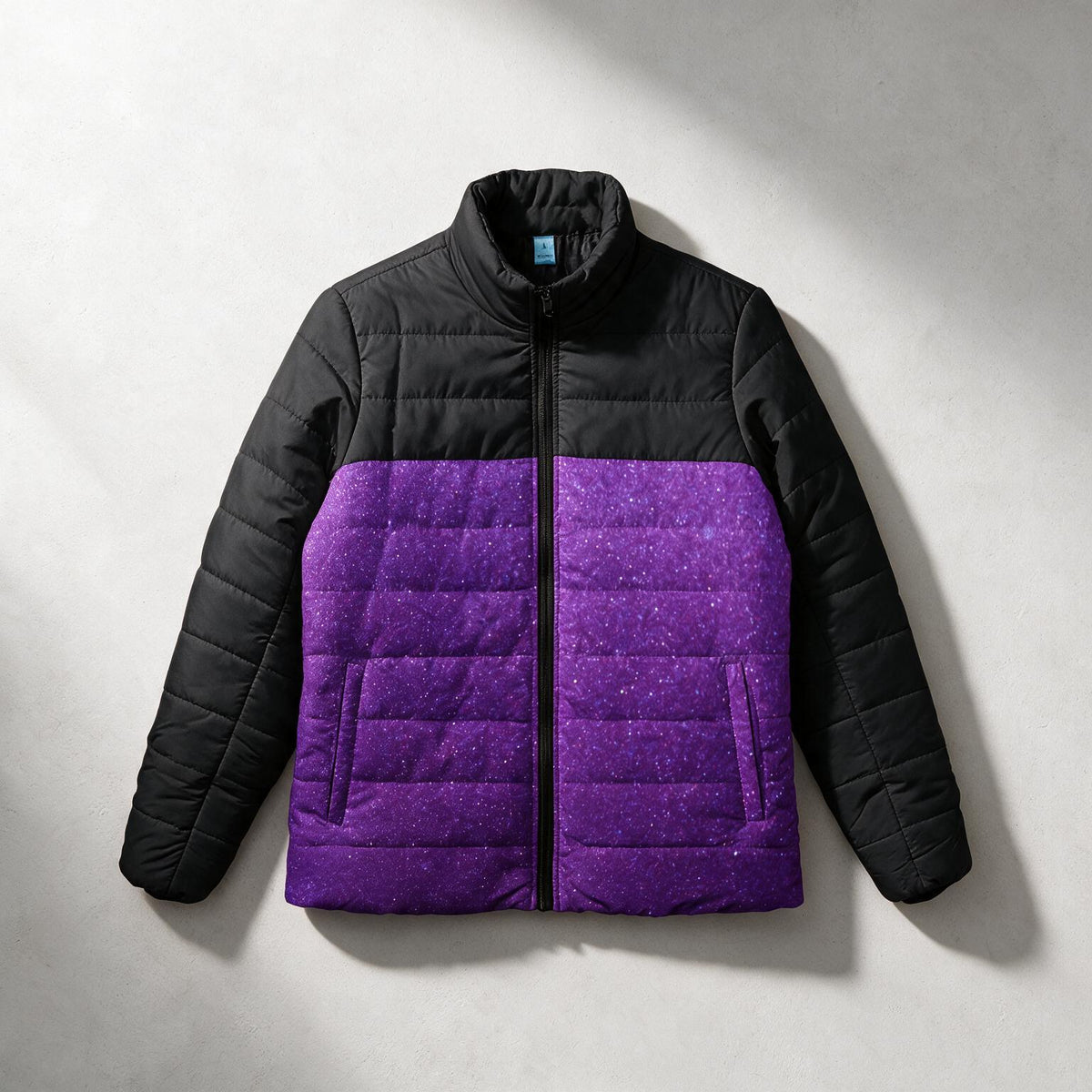 A quilted puffer jacket with a black upper section and sleeves, and a textured purple lower section, laid flat on a light gray background.