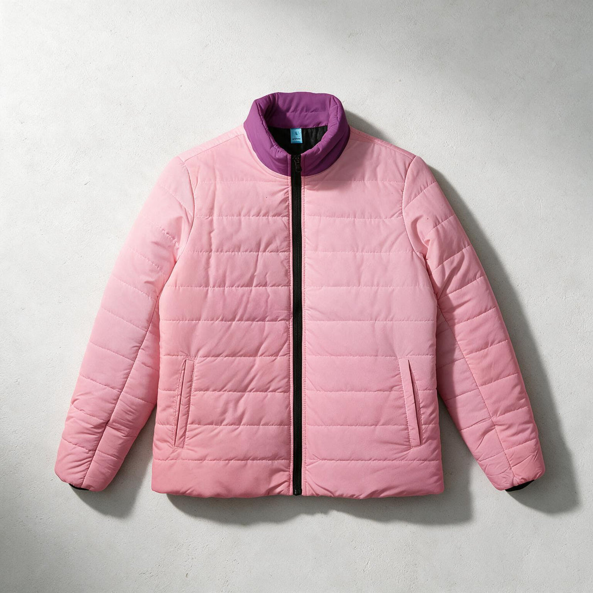 A light pink quilted puffer jacket with a contrasting purple stand-up collar and black zipper, laid flat on a light gray textured background.