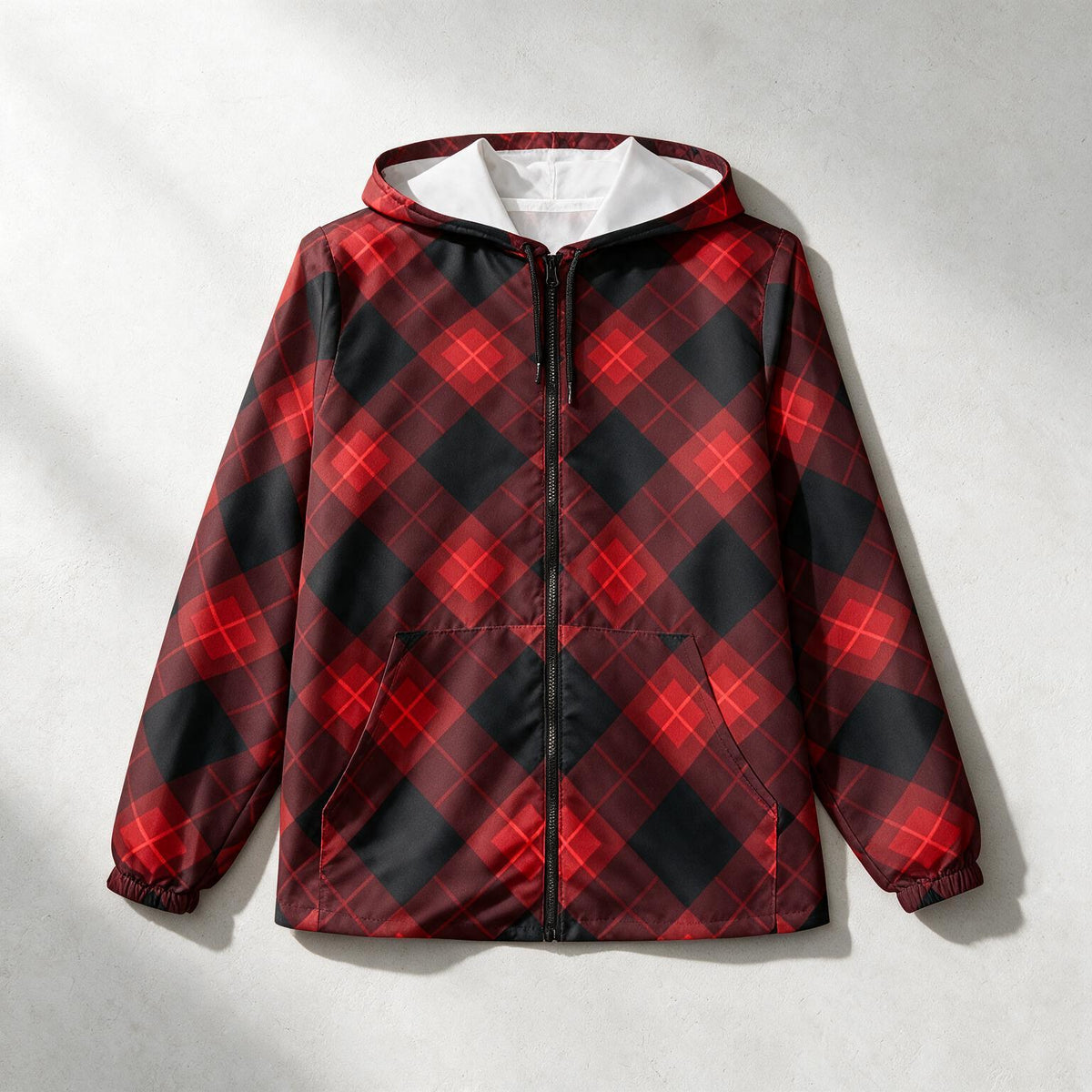 A hooded zip-up jacket with a red and black buffalo plaid pattern, featuring a white hood lining and elastic cuffs, laid flat on a textured light gray background.