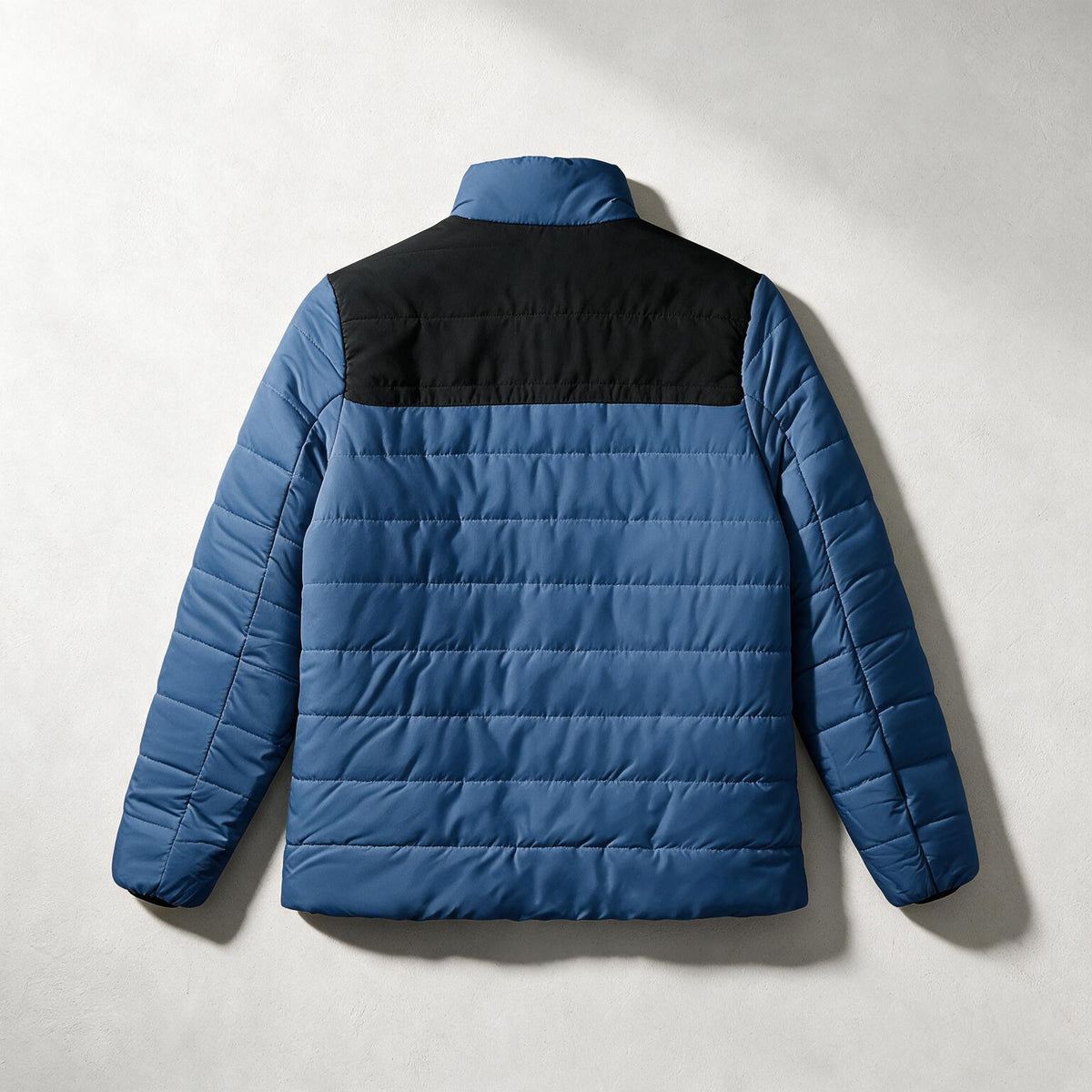 A blue and black quilted puffer jacket shown from the back, laid flat against a light gray textured background.