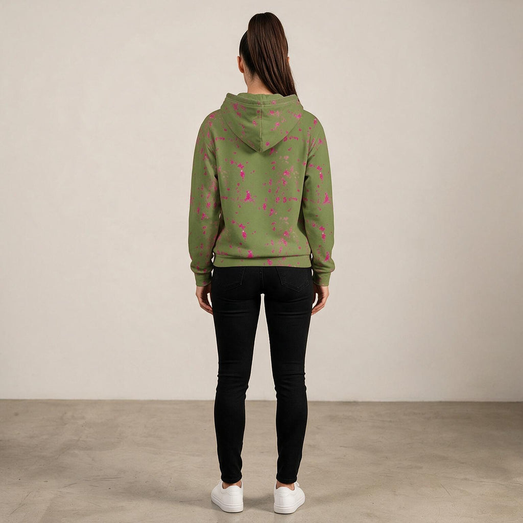 A woman viewed from behind wearing an olive green hoodie with a pink floral pattern, paired with black skinny jeans and white sneakers, standing against a neutral beige wall.