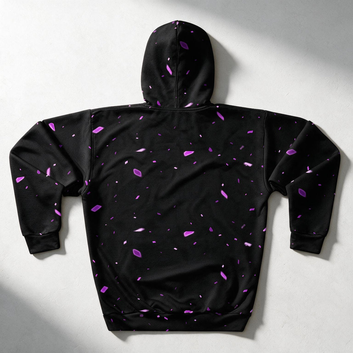 A black hooded sweatshirt shown from the back, featuring a scattered purple and magenta abstract speckle pattern, laid flat on a light gray background with soft shadows.