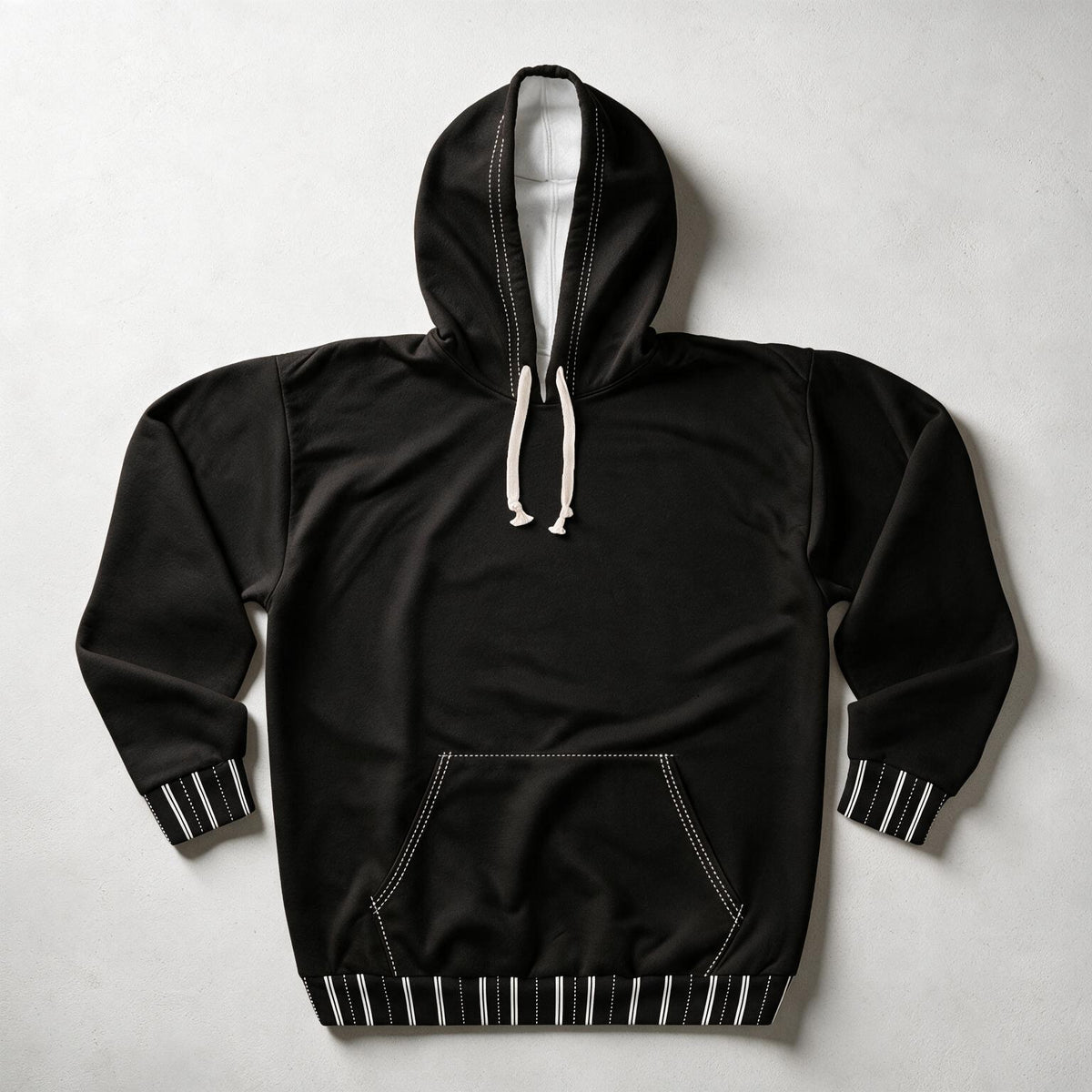 A black pullover hoodie with white drawstrings and contrasting white contrast stitching, featuring striped ribbed cuffs and hem, laid flat on a light gray background.