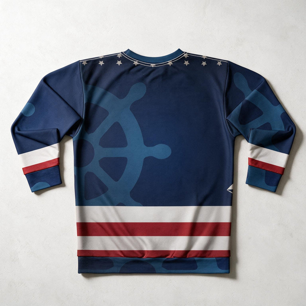 A long-sleeve crewneck shirt laid flat on a light gray background, featuring a navy blue design with a large light blue ship's wheel motif, white stars along the collar, and red and white horizontal stripes near the hem and cuffs.