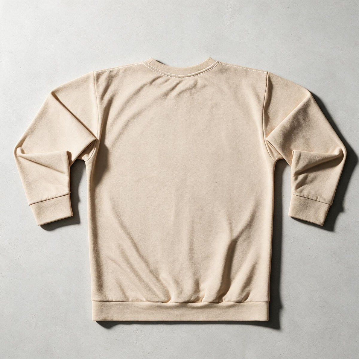 A light beige crewneck sweatshirt shown from the back, laid flat on a textured gray background.