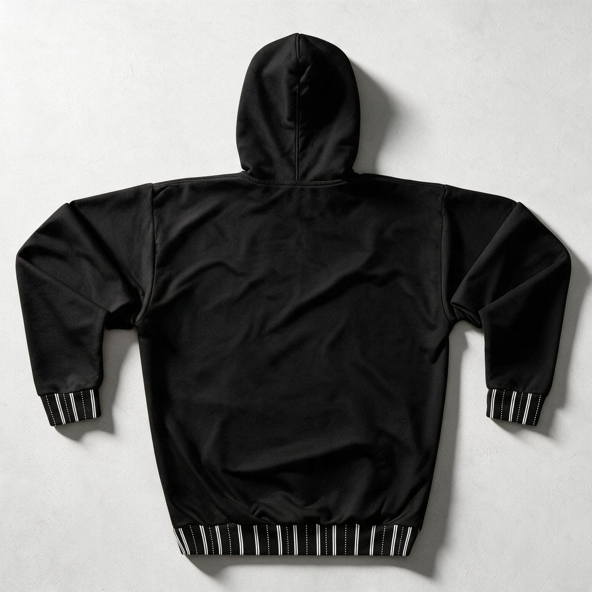 Black hooded jacket shown from the back, laid flat on a light gray background. The sleeves and hem have black-and-white striped ribbed cuffs and hem.
