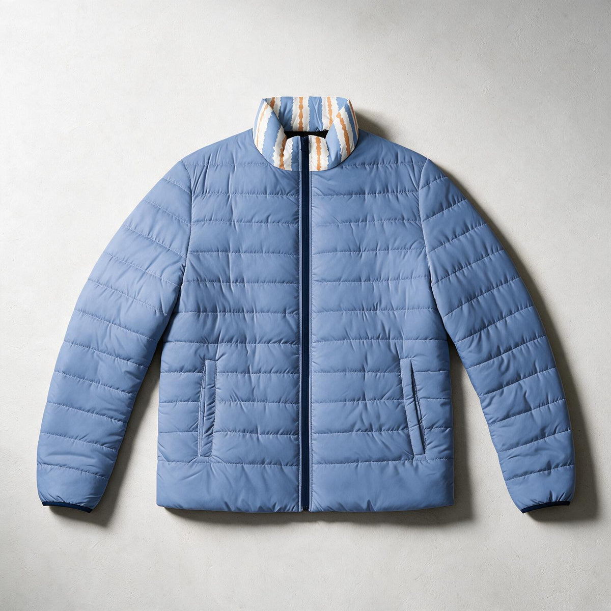 A light blue puffer jacket with a striped collar in blue, white, and orange, laid flat on a light gray background.