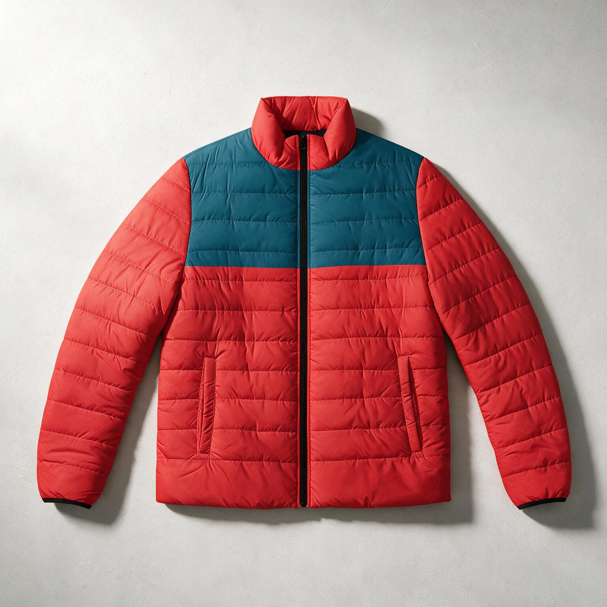 A color-blocked puffer jacket with a red body and sleeves, and a teal blue yoke across the chest, laid flat against a light gray background.