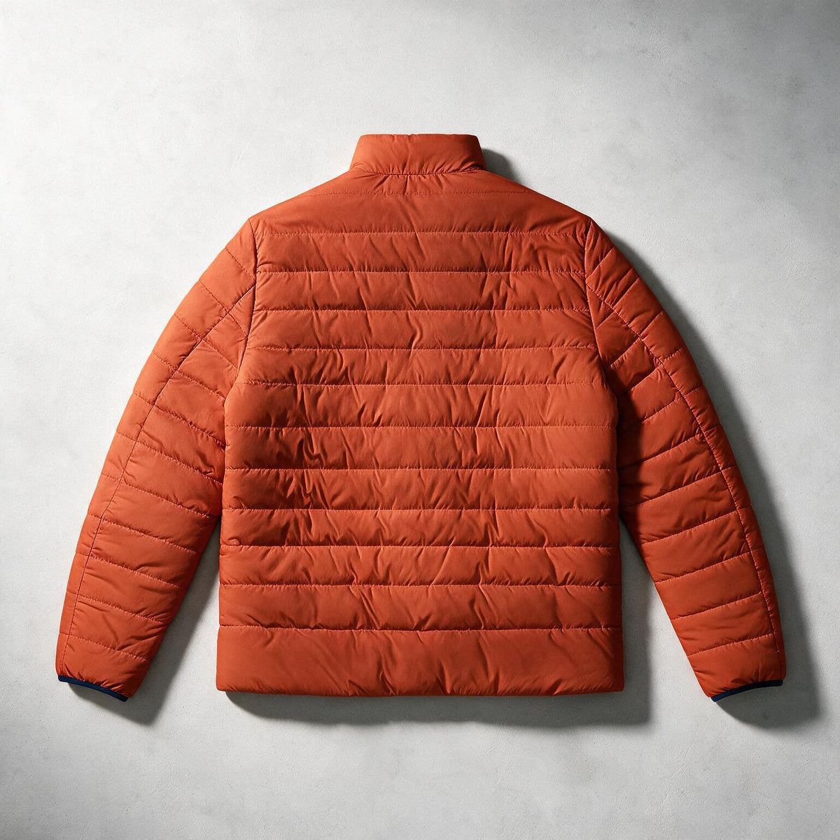 An orange quilted puffer jacket shown from the back, laid flat on a textured light gray background.