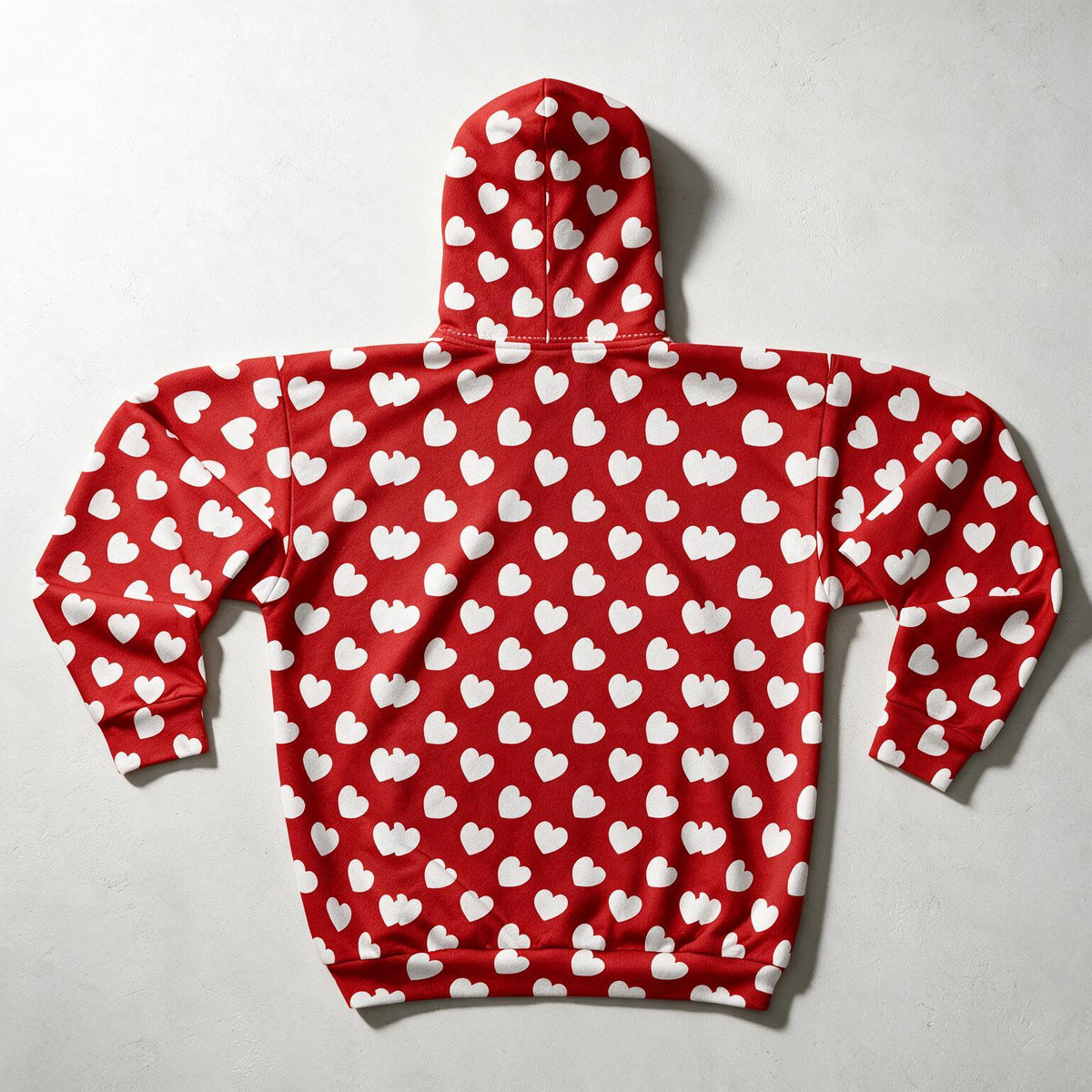 A red hooded sweatshirt with an all-over white heart pattern, laid flat on a light gray textured background.