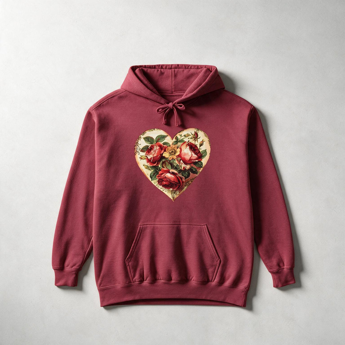 A maroon pullover hoodie with a vintage-style heart graphic on the chest containing red roses and green leaves, laid flat on a light gray textured background.