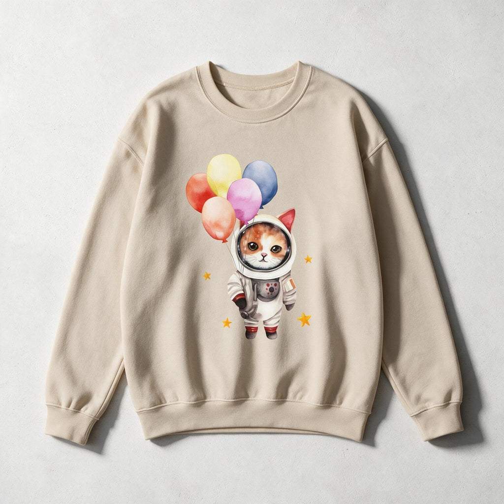 A beige crewneck sweatshirt featuring a cute graphic of a cat dressed as an astronaut holding colorful balloons, displayed flat against a light gray textured background.