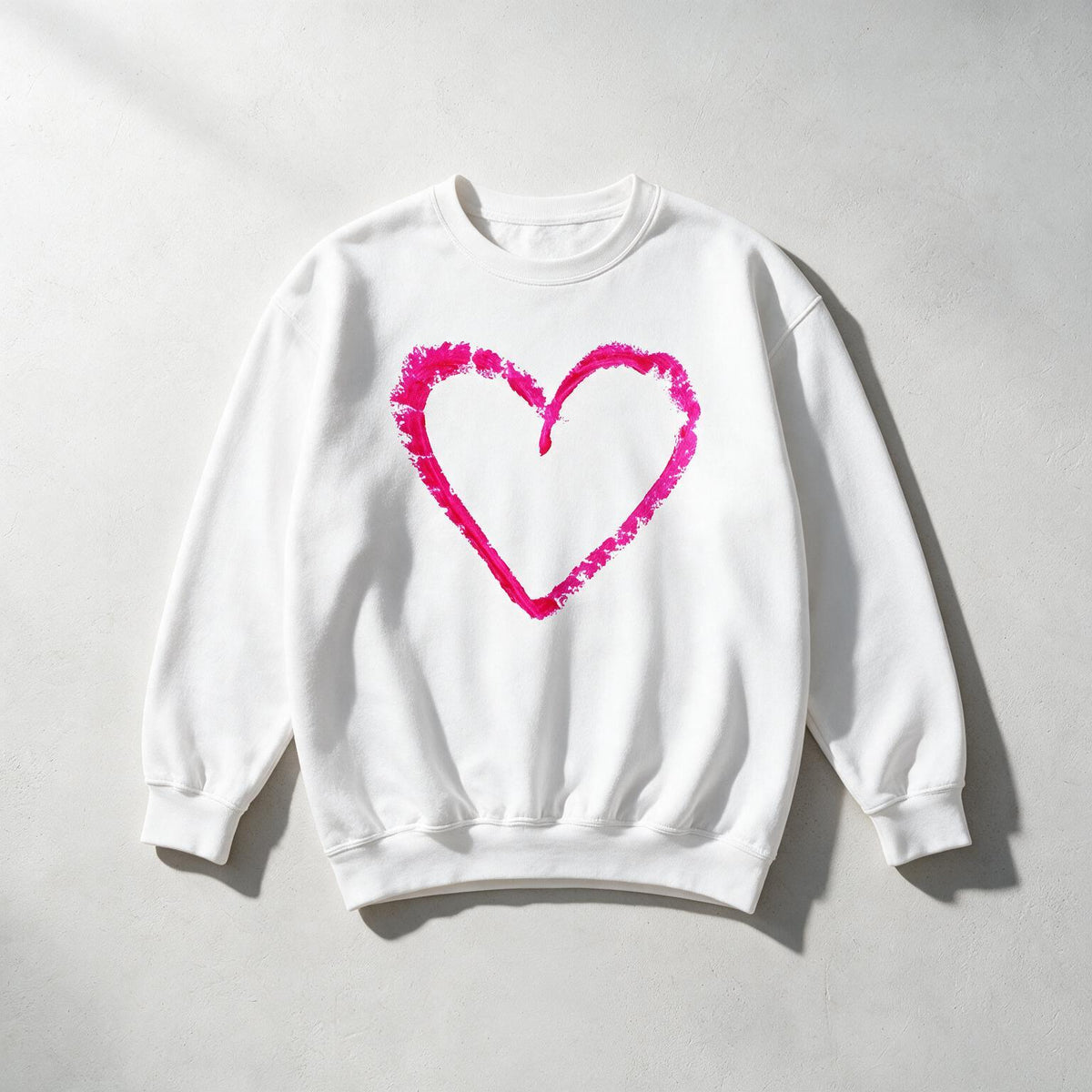 A white crewneck sweatshirt with a vibrant pink textured heart outline printed on the chest, laid flat on a light gray background.