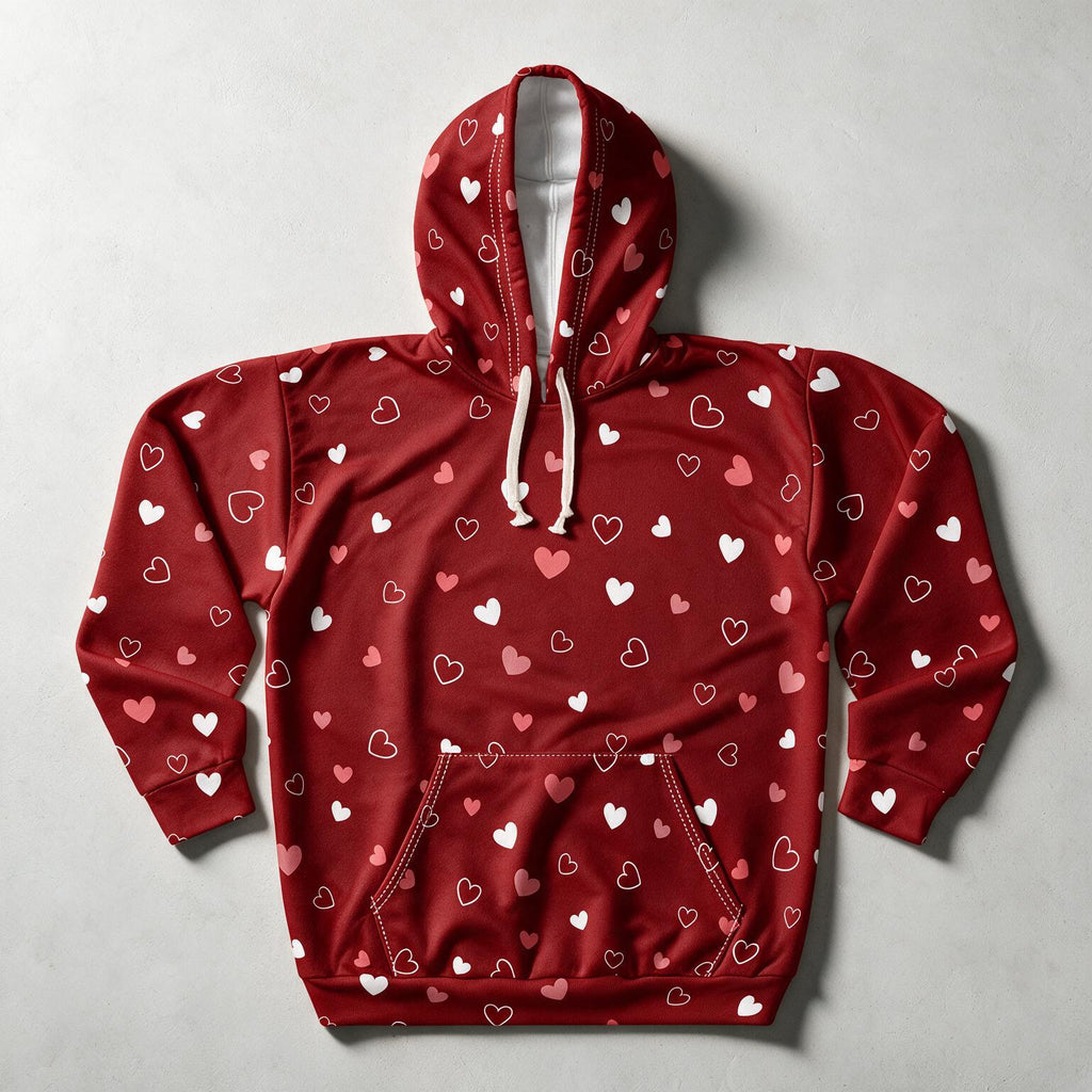 A red pullover hoodie with an all-over pattern of small white and pink hearts, featuring cream-colored drawstrings and a front kangaroo pocket, laid flat on a light gray background.