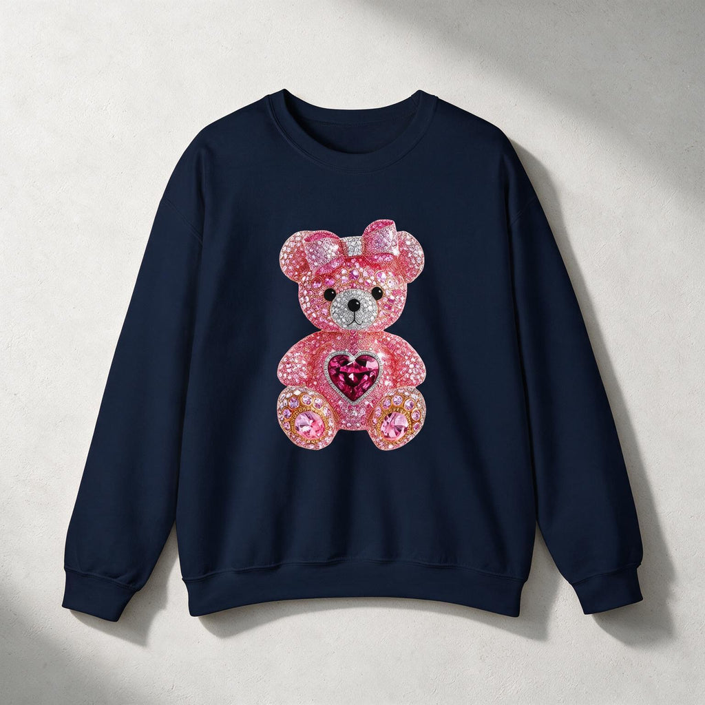 A navy blue crewneck sweatshirt featuring a large pink rhinestone teddy bear graphic on the front, set against a textured light gray background with soft diagonal shadows.