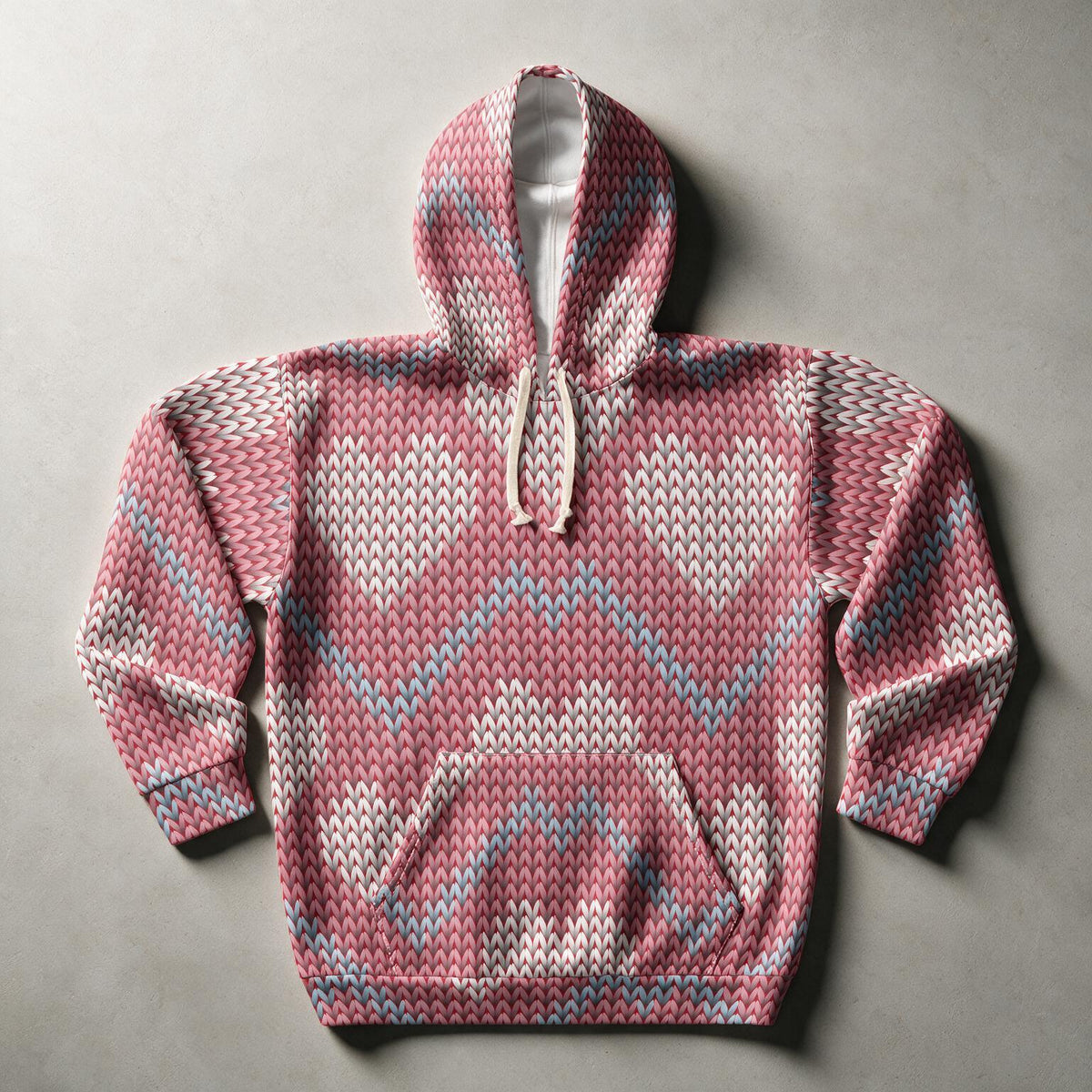 A pink knit hoodie with a textured geometric pattern in white and light blue, laid flat on a neutral gray background.