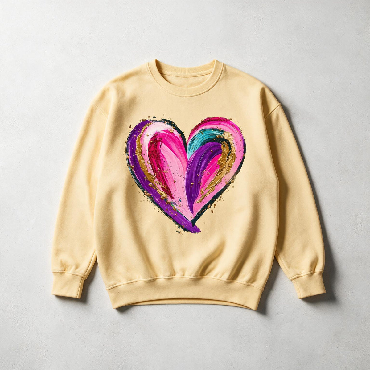A pale yellow crewneck sweatshirt with a large, colorful abstract heart graphic on the front, laid flat on a light gray textured background.