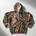 A hooded sweatshirt laid flat on a light gray surface, featuring an all-over jungle and safari print with giraffes, zebras, leopards, and tropical leaves in green, red, brown, and beige tones.