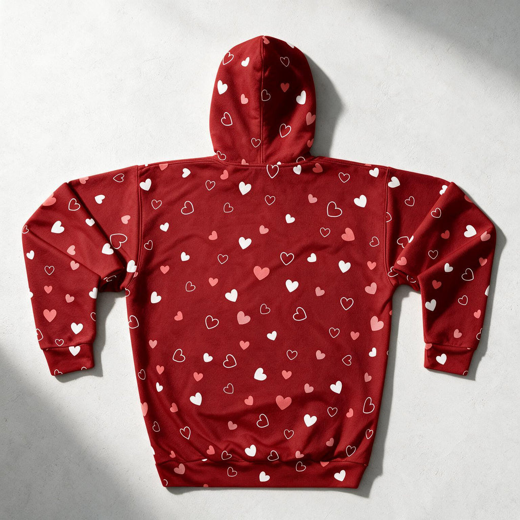 A red pullover hoodie with an all-over heart pattern, shown from the back on a light gray textured background with soft shadows.