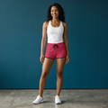Woman wearing a white tank top and pink shorts against a blue background