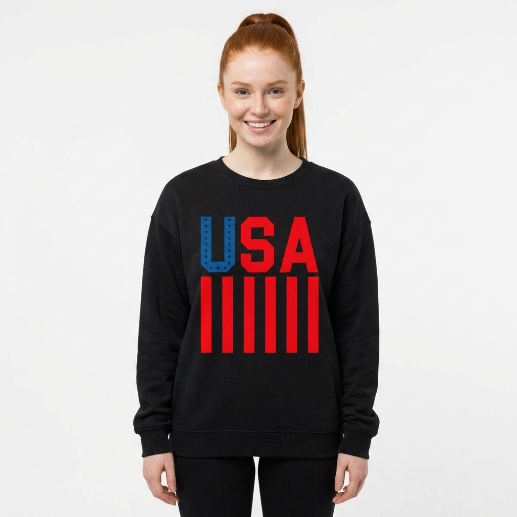 A woman with red hair in a ponytail wearing a black crewneck sweatshirt with a red and blue 'USA' graphic and red stripes on the front, set against a plain light gray background.